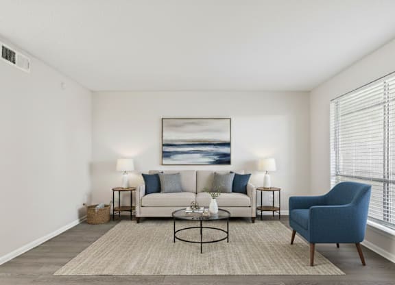 A living room with a white couch, a blue chair, and a painting on the wall.