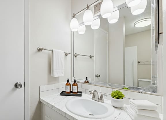 A white bathroom with a sink, mirror, and lights.
