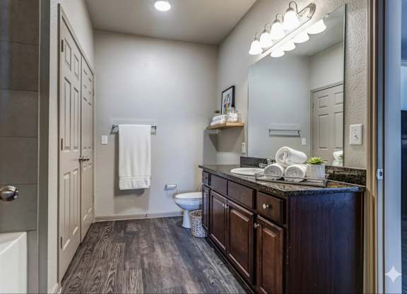 A bathroom with a wooden floor and a white towel hanging on the door.