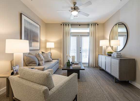A well-lit living room with a grey sofa, two chairs, and a coffee table.