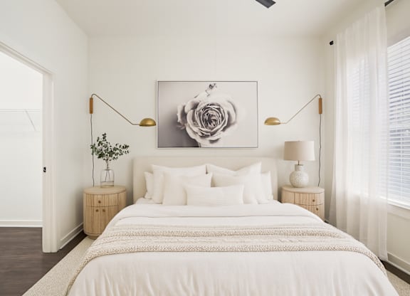 A bedroom with a large bed, a painting above it, and two lamps on either side of the bed.