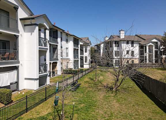 A row of white apartment buildings with black fences and green bushes.