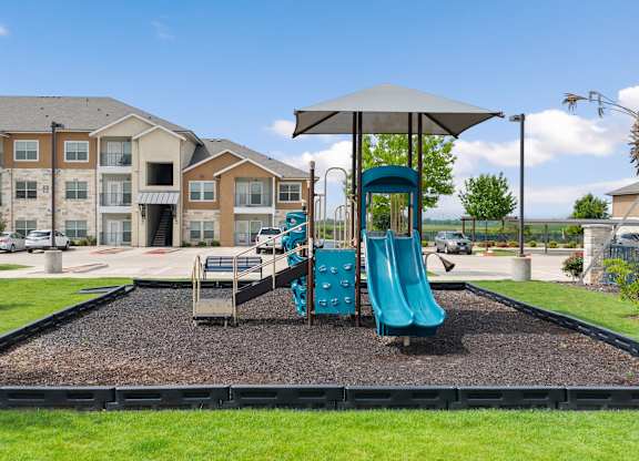 A playground with a blue slide and a brown building in the background.