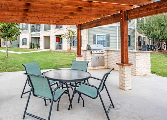 A patio with a table and chairs under a wooden pergola.