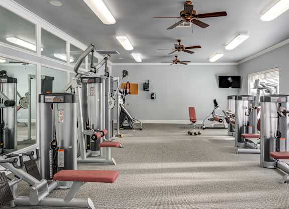 A well-equipped gym with various machines and a ceiling fan.