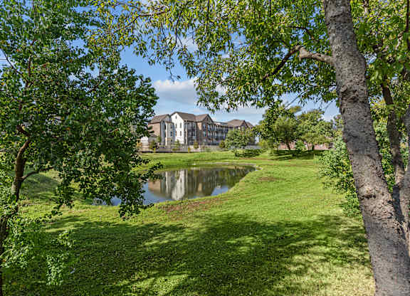 A serene landscape with a pond, trees, and a building in the distance.