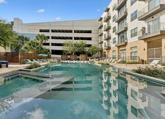 A swimming pool in front of a building with a parking garage.