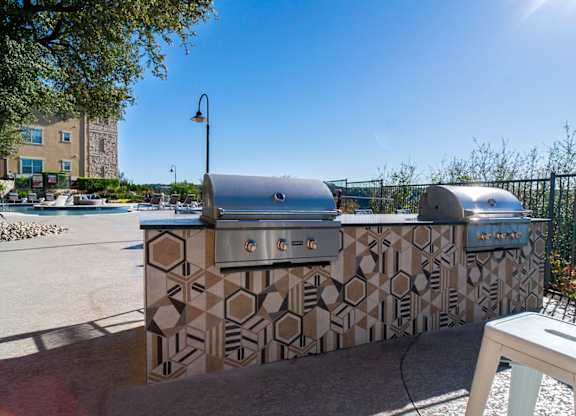 A large outdoor kitchen with a patterned tile backsplash and a grill.