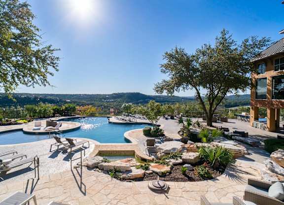 A large outdoor swimming pool surrounded by a stone patio and lounge chairs.