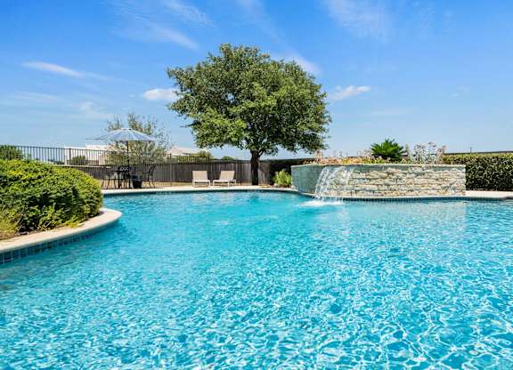A pool with a waterfall and a tree in the background.