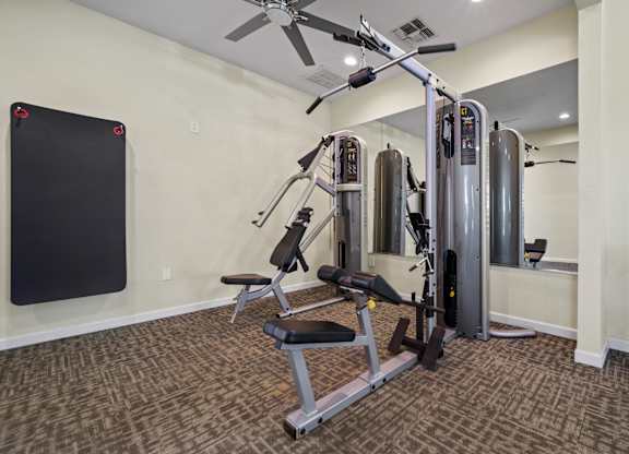 A home gym with a weight machine, a bench, and a fan.