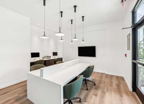 A white desk with green chairs and hanging lights in a room.