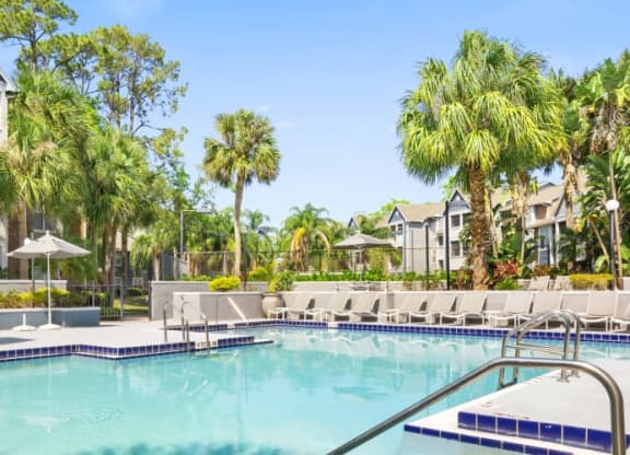 a large swimming pool with chaise lounge chairs and palm trees in front of a building