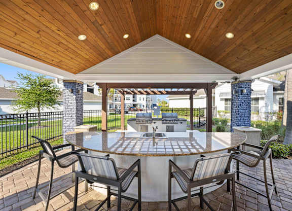 a patio with a large circular table and chairs with a grill in the background