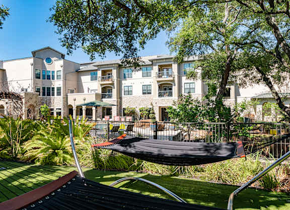 A hammock is suspended between two trees in a backyard.