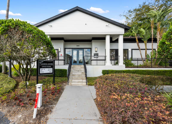 the front of a white building with a sidewalk and a black sign