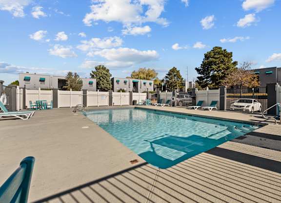 a swimming pool at an apartment complex with chairs and a privacy fence