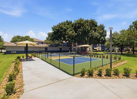 A tennis court is surrounded by a fence and a building.