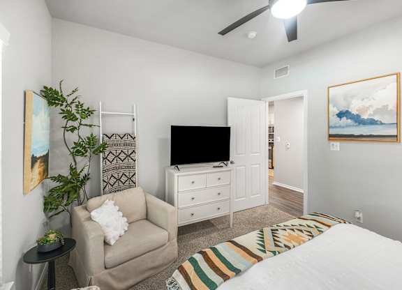 A bedroom with a bed, chair, and television.