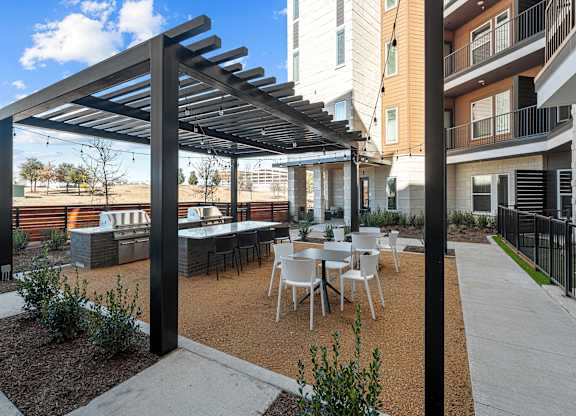 A patio with a table and chairs under a black pergola.