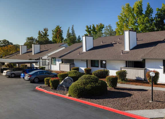 A parking lot in front of a building with a white fence and a red line painted on the ground.