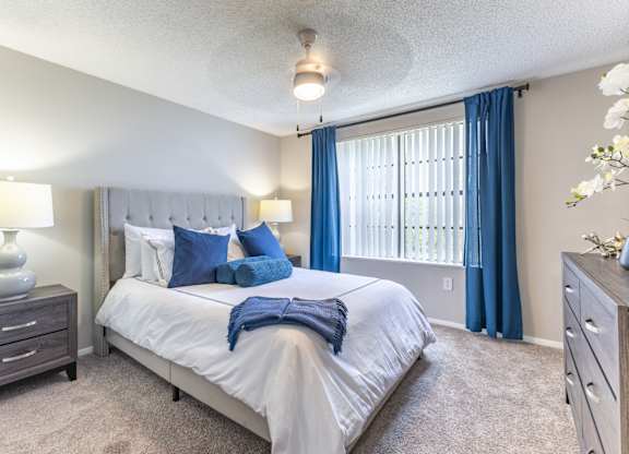 A bedroom with a large bed, a nightstand, and a window with blue curtains.