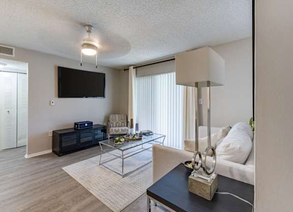 A living room with a black sofa, a glass coffee table, and a television mounted on the wall.