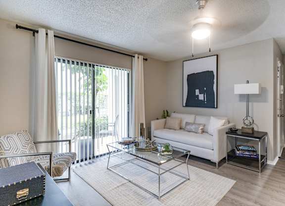 A living room with a white couch, a coffee table, and a large window with curtains.