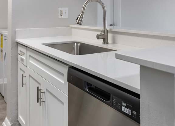 A modern kitchen with a stainless steel dishwasher and white countertops.