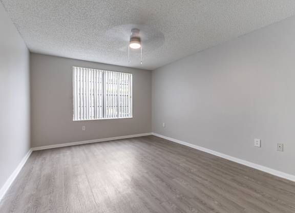 A room with a window covered by blinds and wooden flooring.