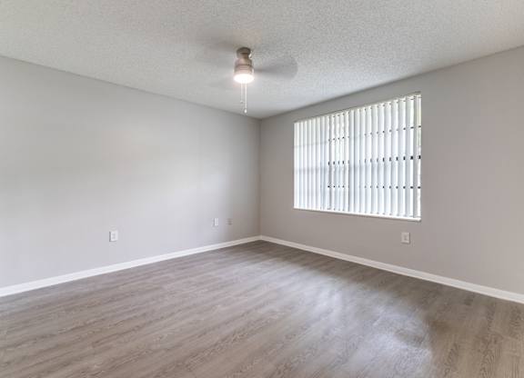 A room with a window covered by blinds and wooden flooring.