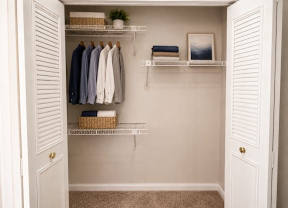A white closet with clothes hanging and shelves with towels and a plant.
