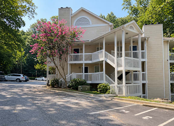 A two-story building with a balcony and a tree with pink flowers in front.