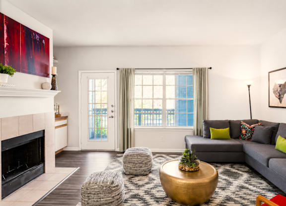 A living room with a grey couch, a fireplace, and a large window.