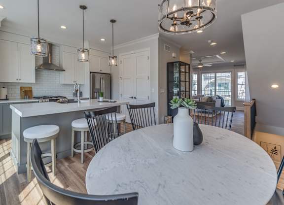 A modern dining room with round marble table and chairs with a  modern builder grade kitchen in the background,