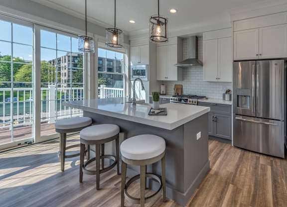 A  modern builder grade kitchen with an island with farmhouse sink and eating with with sliding glass doors in the background leading to an outdoor balcony.