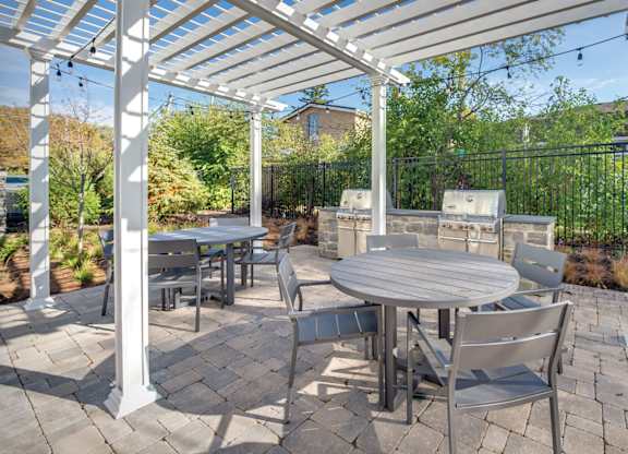 A townhome complex patio with grills, tables and chairs on a brick walkway underneath cafe lights.
