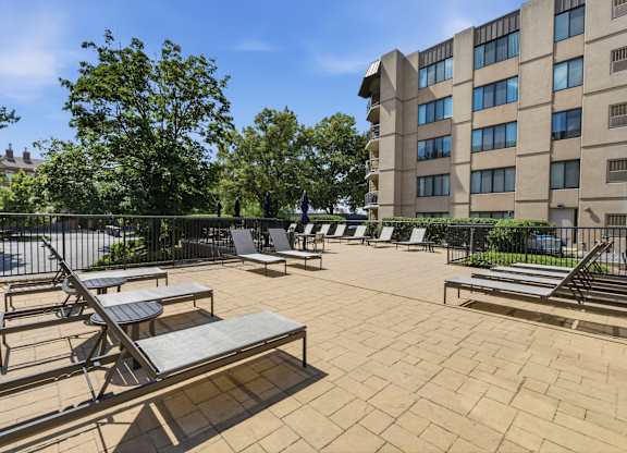 A sunny day at the outdoor seating area of a building with multiple lounge chairs and tables.