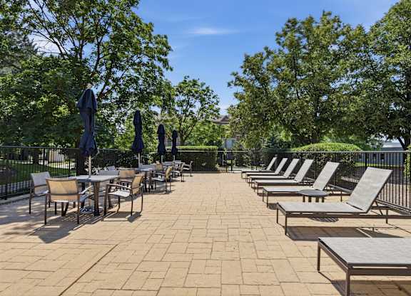 A patio with chairs and tables is surrounded by trees.