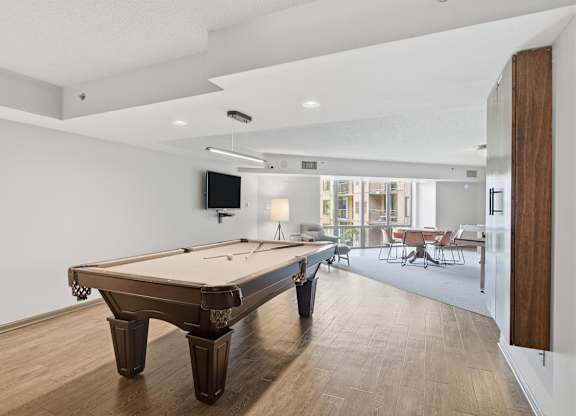 A pool table is in the middle of a room with a TV and chairs.