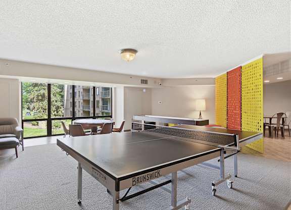 A ping pong table is in the middle of a room with a chair and a window.