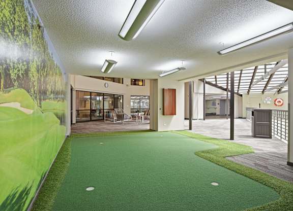 A room with a green carpet and a wall mural of a golf course.