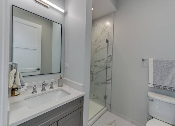 A modern builder grade bathroom with a white toilet, marble counter top vanity, and glass tiled shower.