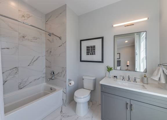 A modern builder grade bathroom with a marble tile shower with soaking tub, white toilet, and vanity with mirror.