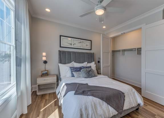 A modern builder grade bedroom with a large bed, ceiling fan, large closet, and window.