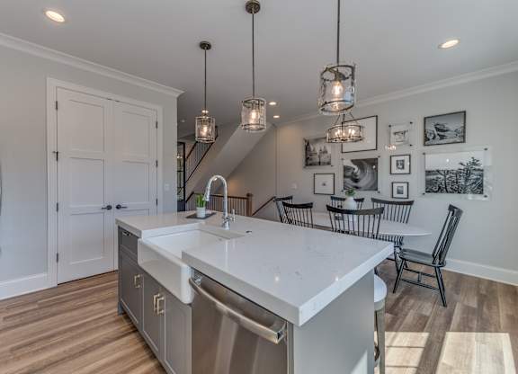 A modern builder grade kitchen island with a farmhouse sink and eating bar with a double door pantry and dining room in the background.