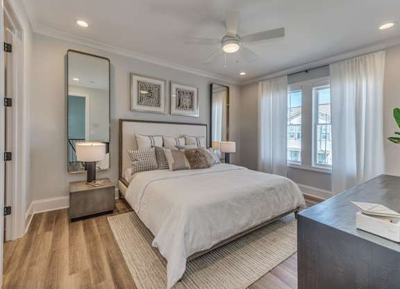A modern builder grade bedroom with a large bed, windows, a ceiling fan, and dual side tables with lamps.