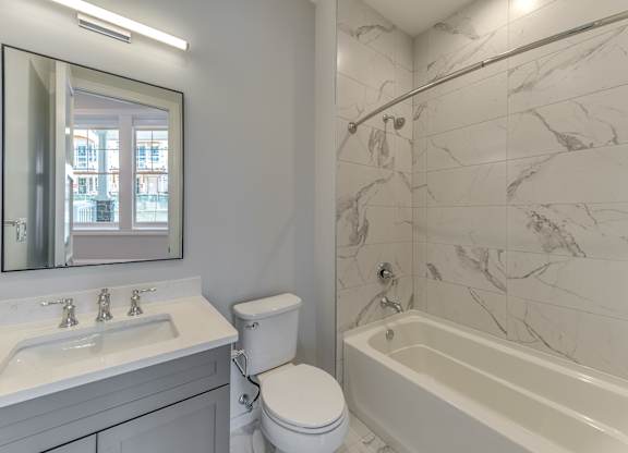 A modern builder grade bathroom with a marble tile shower and soaking tub with vanity and mirror.