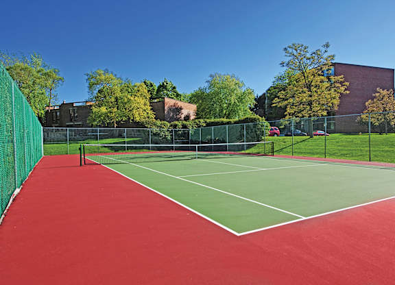 A tennis court with a red surface and green fencing.