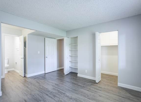 A room with white walls and wood flooring with a doorway leading to another room.